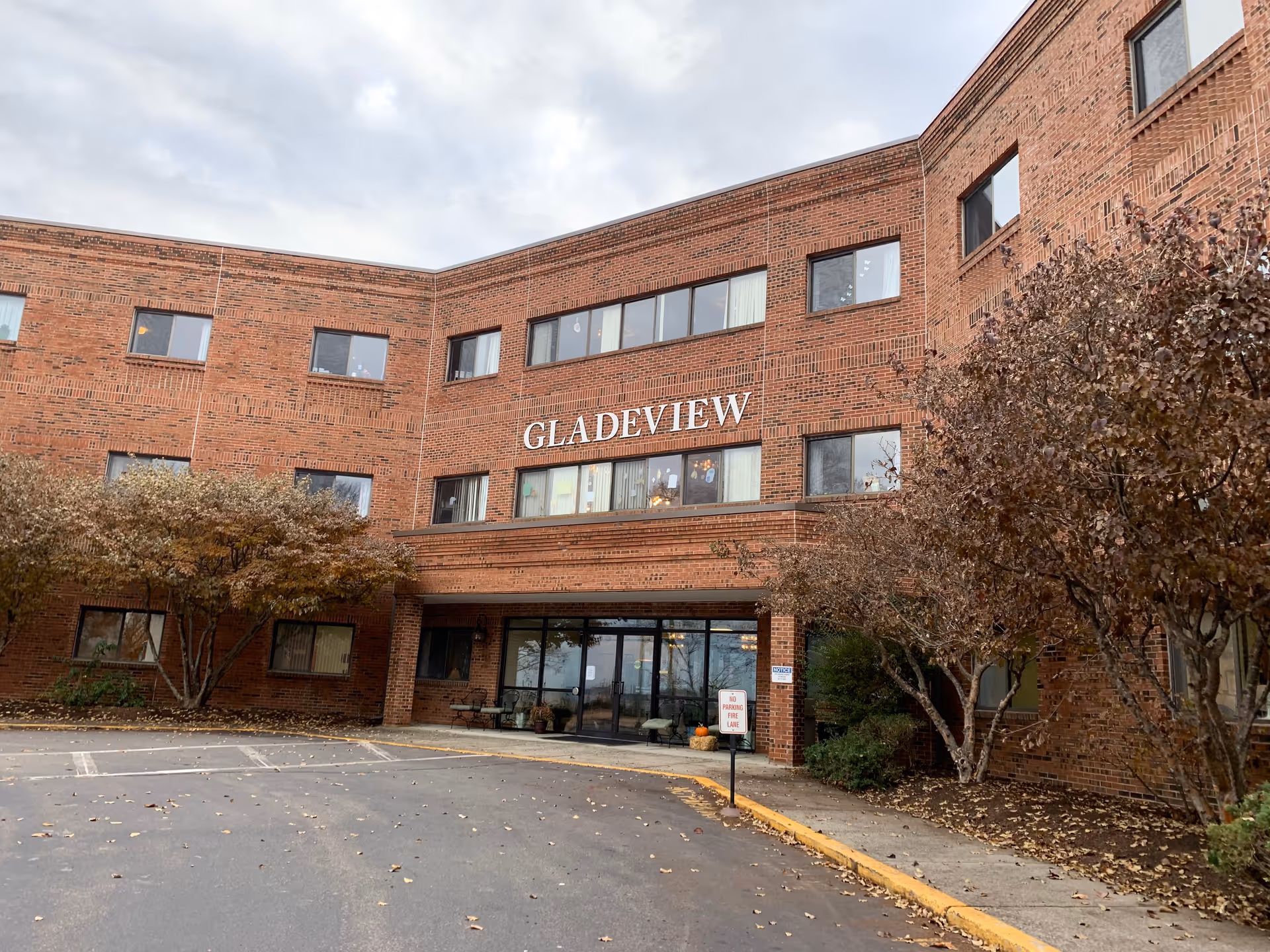 Brick Gladeview senior living facility with a glass entrance and leafless trees.