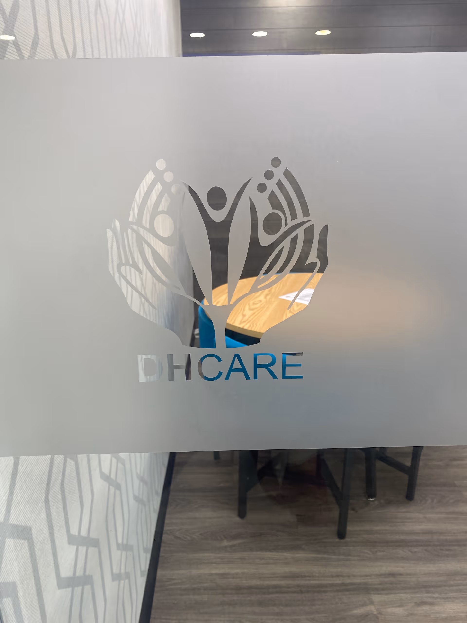 Frosted glass panel with the DHCARE logo, revealing a wood-floor interior behind.