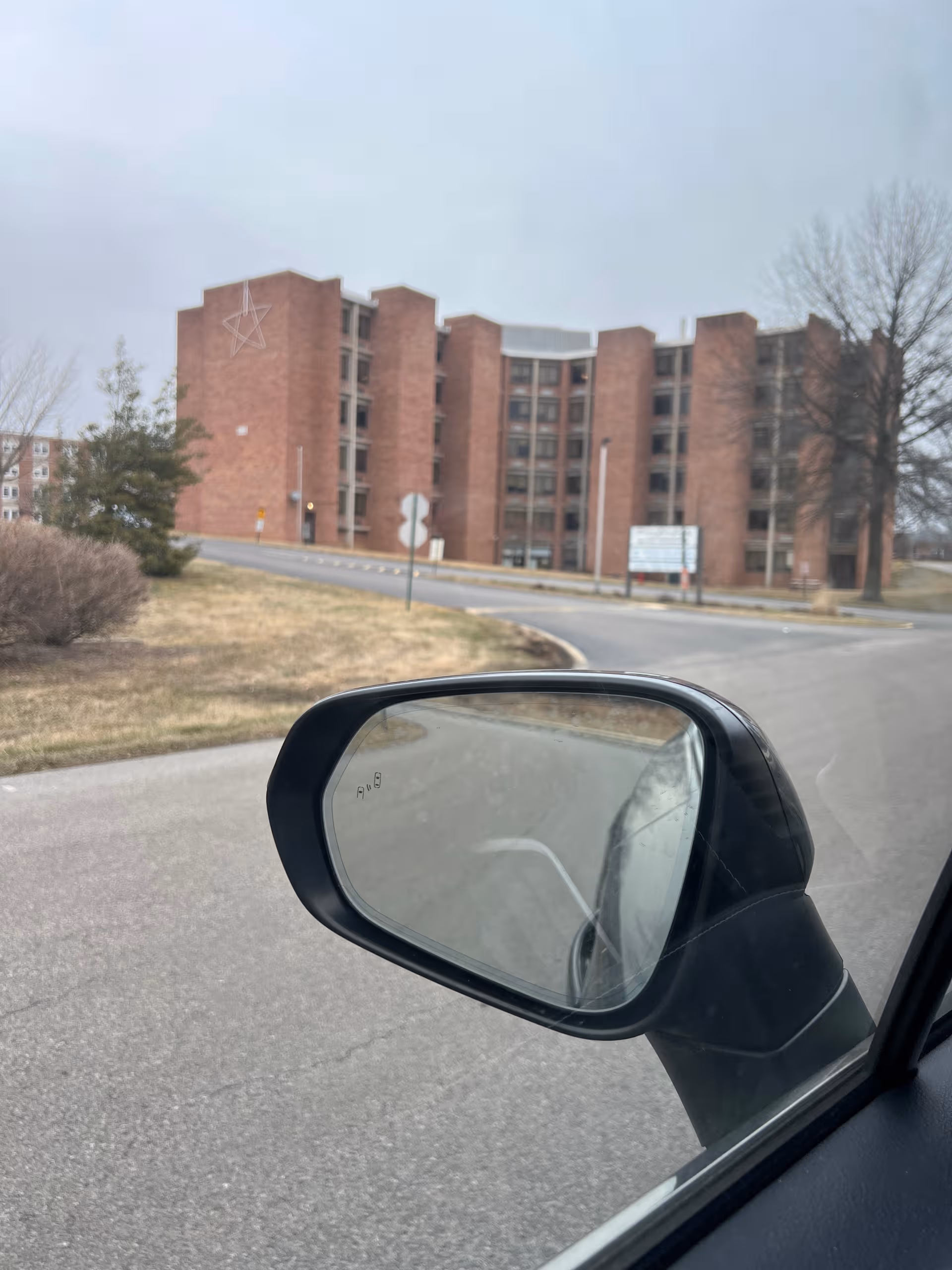Brick Pleasant Acres exterior viewed from road, with a car mirror in foreground.