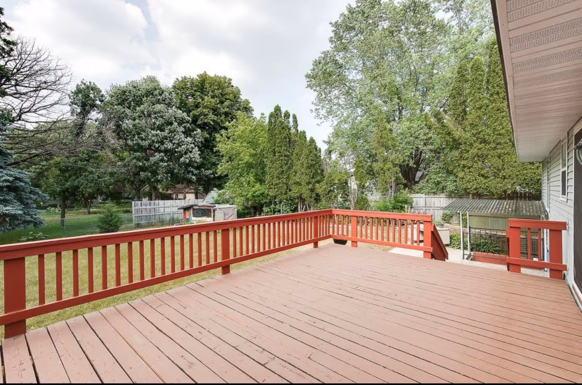 Large wooden deck with red railing extends from a house into a grassy backyard.