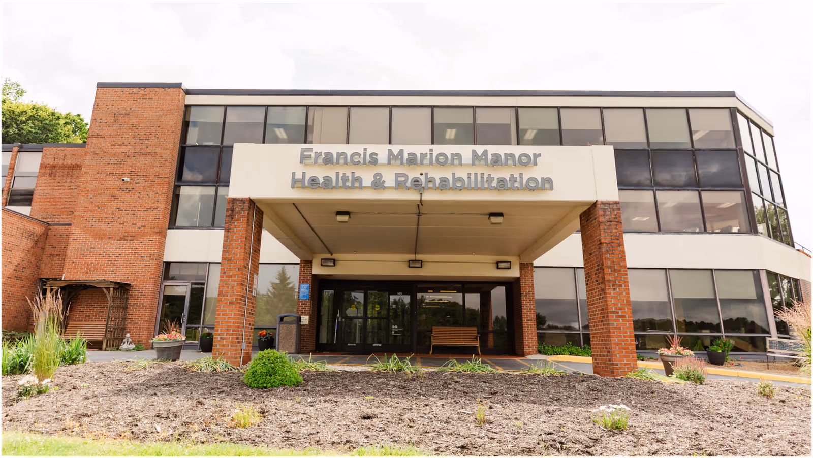 Front view of Francis Marion Manor Health & Rehabilitation entrance with brick pillars and glass windows.