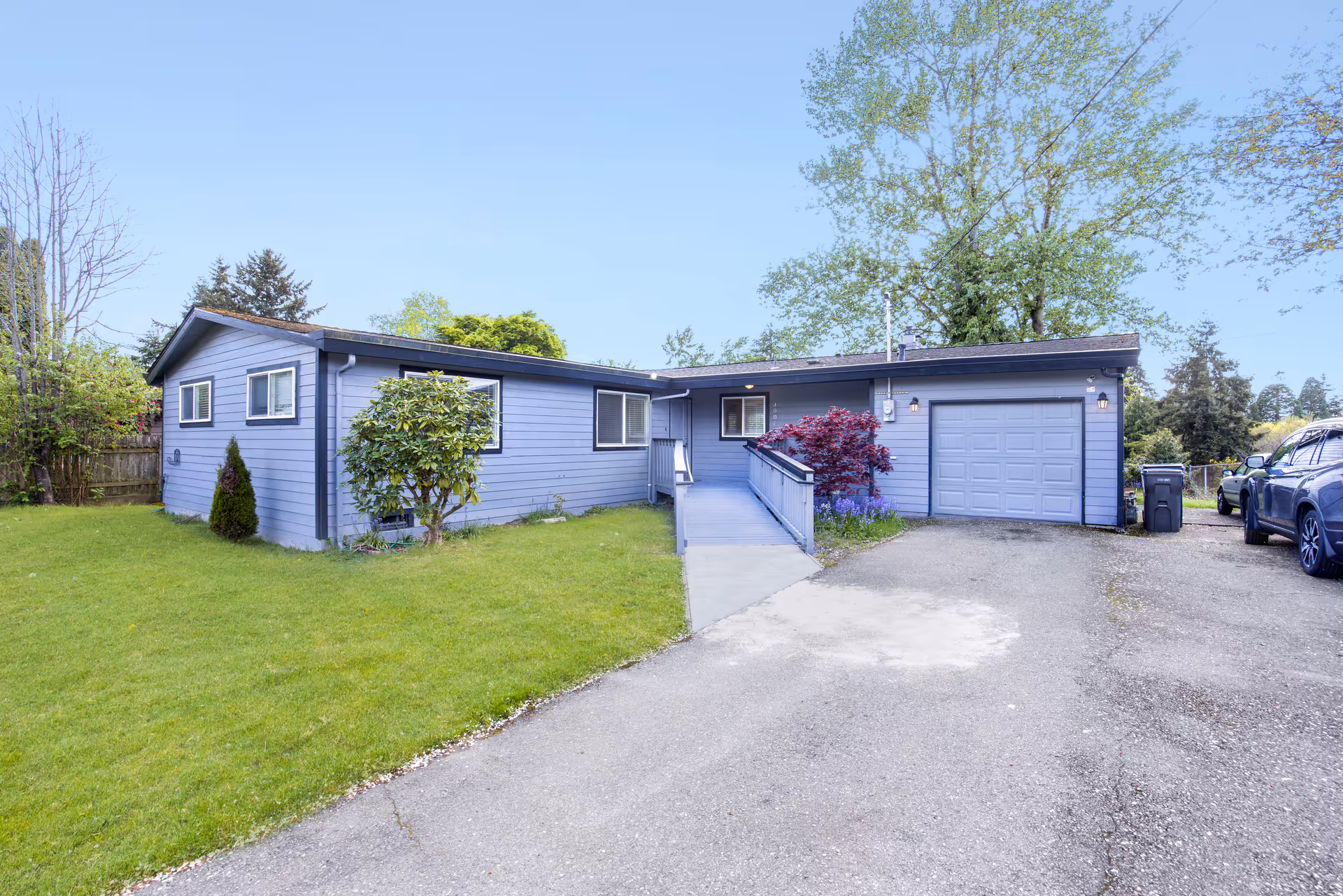 Blue single-story residence with a ramp, attached garage, and well-kept lawn.