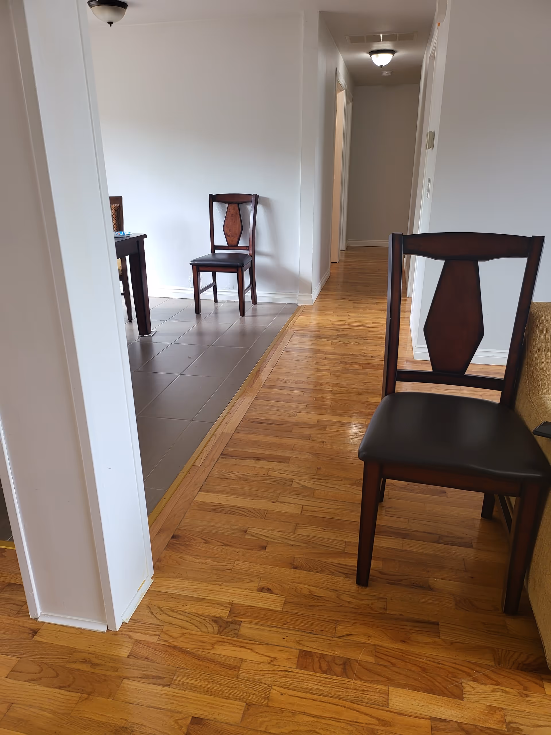 Interior hallway of a senior living facility with wooden floors and chairs along the wall.