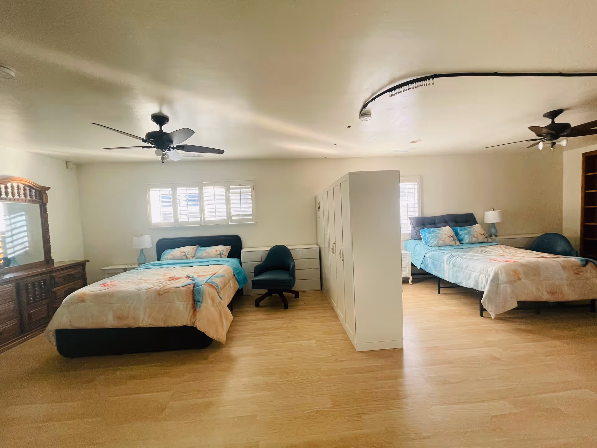 Bright shared bedroom with two beds, a central partition, dresser, and ceiling fans.
