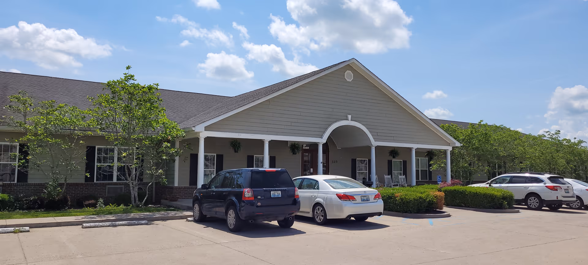 Arcadian Cove Senior Living facility exterior with arched entrance and parked cars.