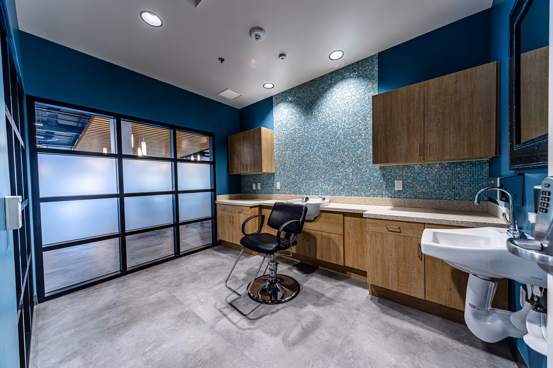 Modern interior featuring a sink, hair chair, wood cabinets, and blue mosaic backsplash.