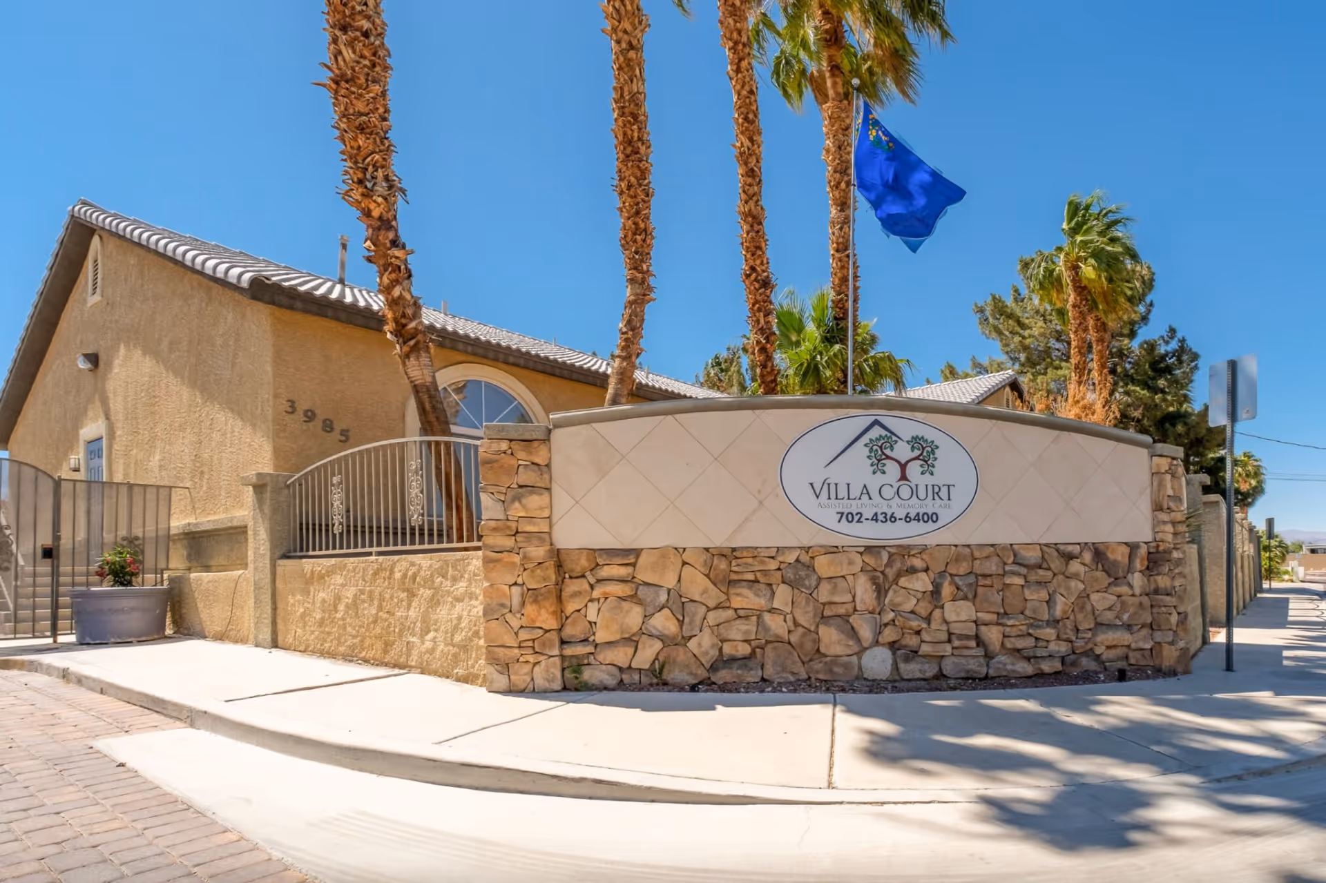 Front exterior view of Villa Court Assisted Living entrance with stone wall and palm trees