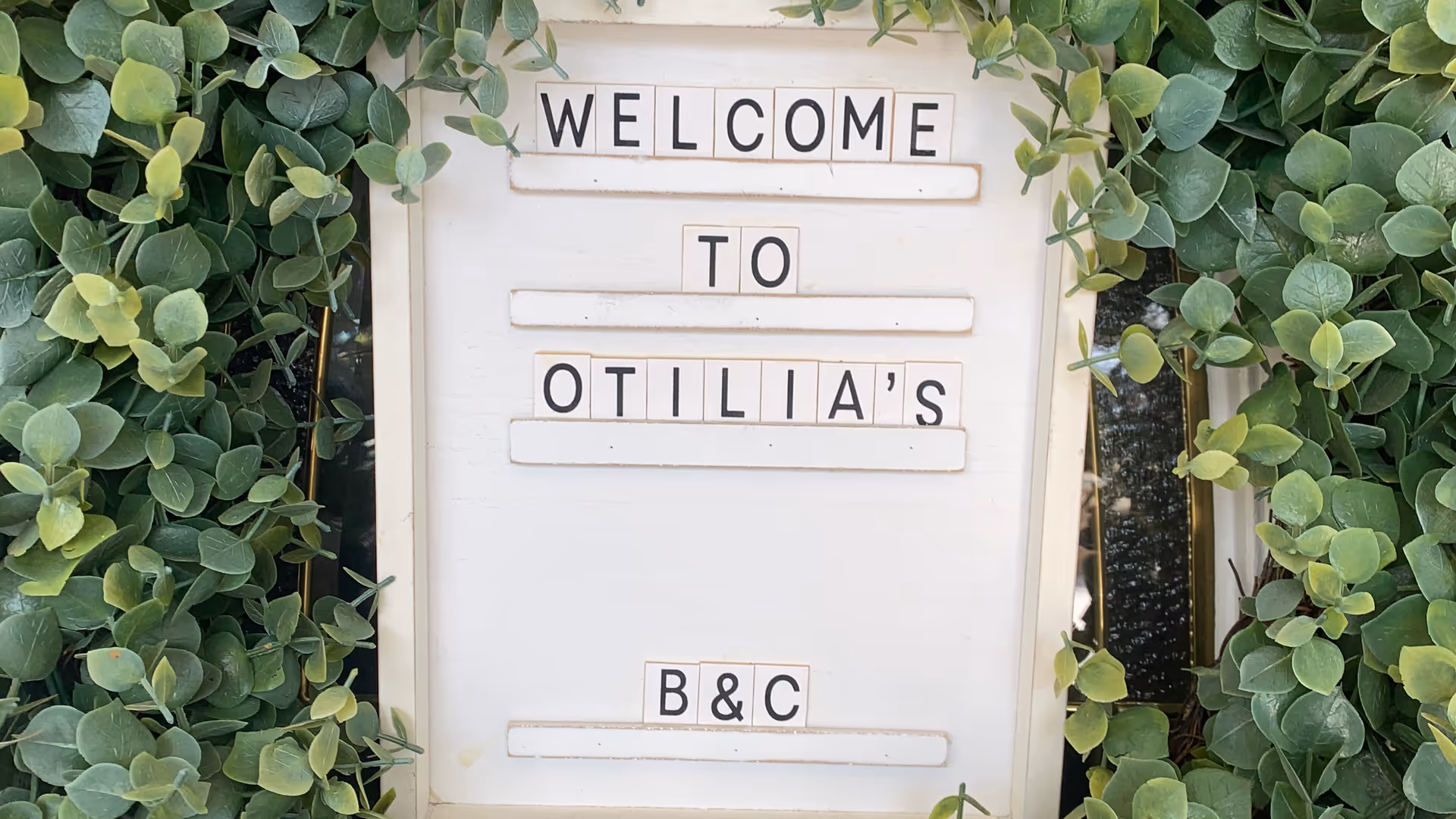 A welcome sign reading 'Welcome to Otilia's B&C' framed by green vines.