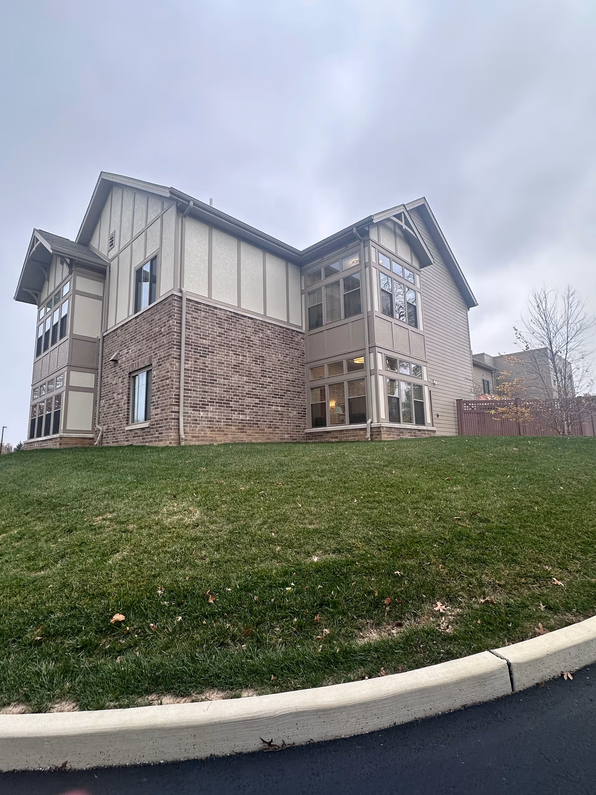 Two-story brick-and-siding senior living building on a grassy slope under a cloudy sky.