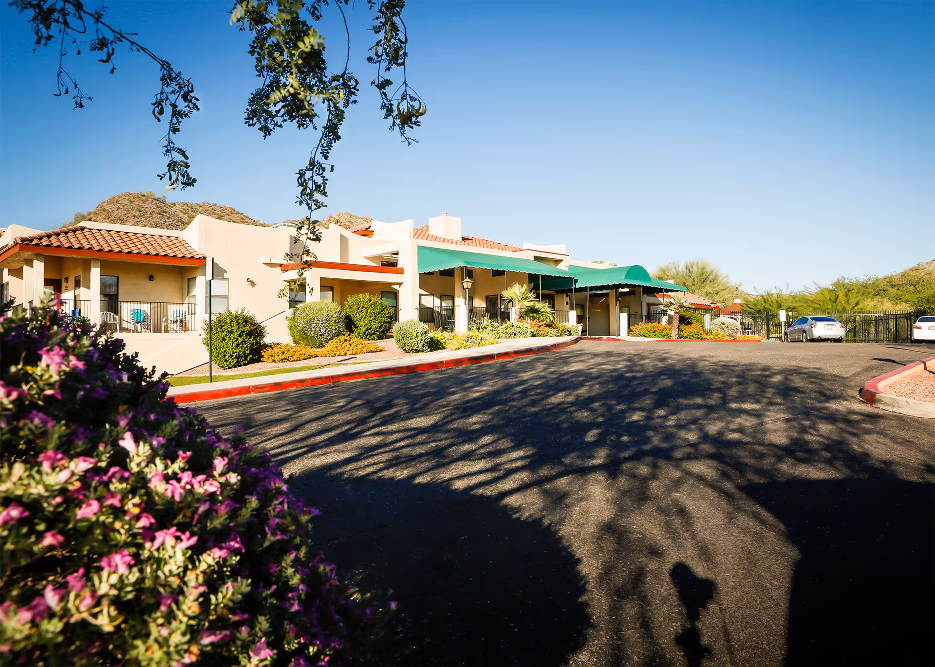 Exterior view of Bethesda Gardens facility with beige buildings, green awnings, and parked cars.