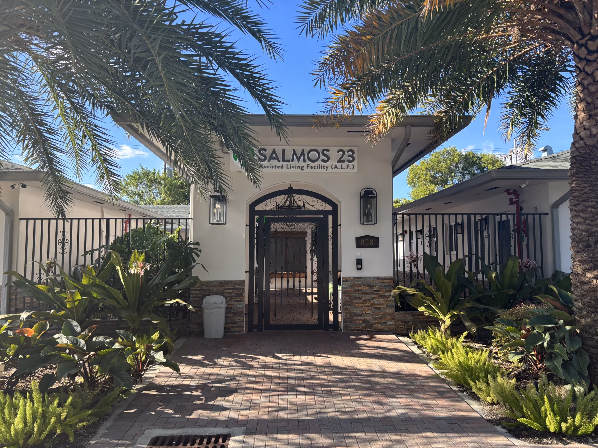 Entrance of ALF Salmos 23 No.3 with gate, lush plants, and palm trees.