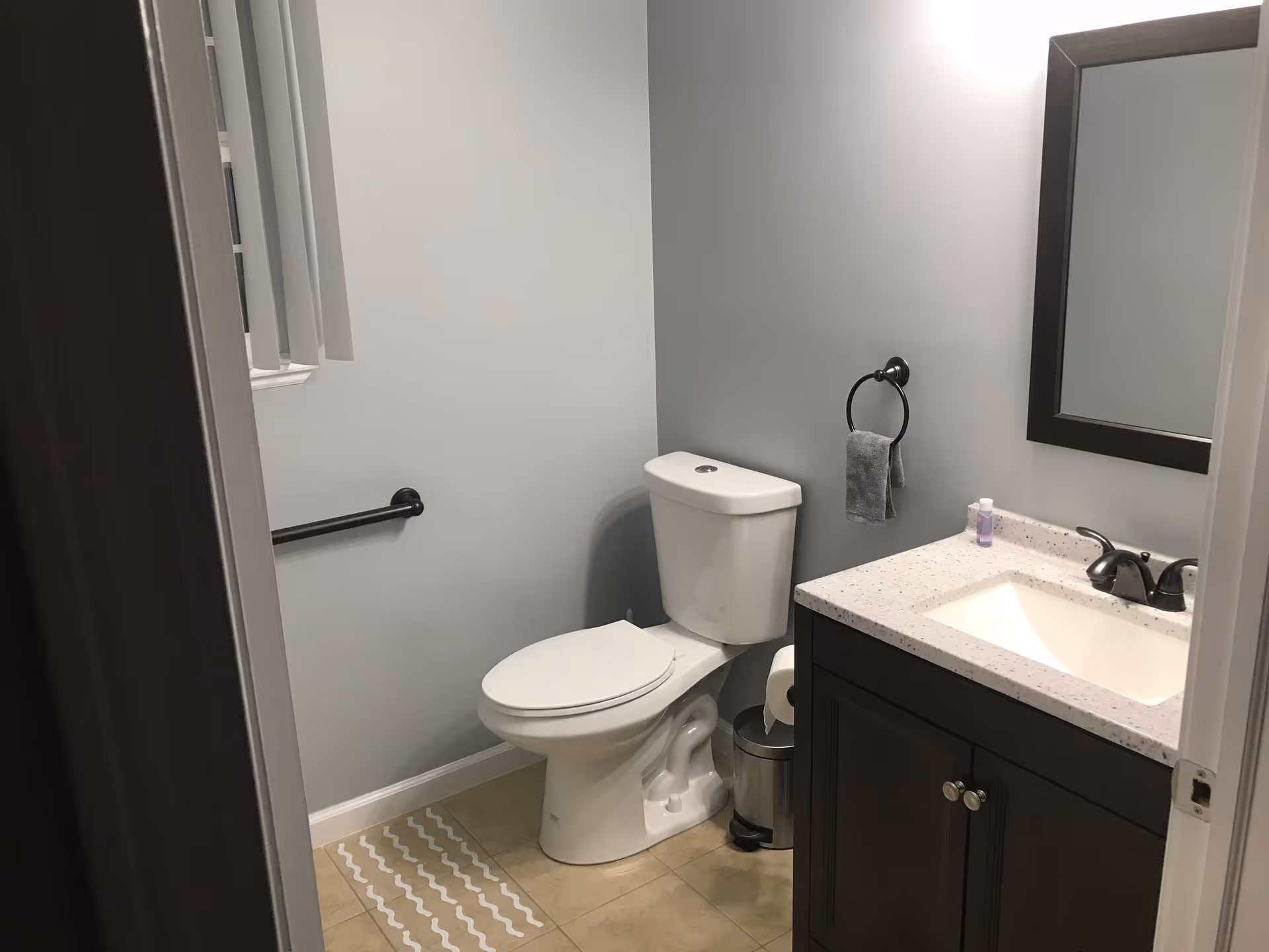 Clean bathroom with toilet, sink, mirror, and towel ring.