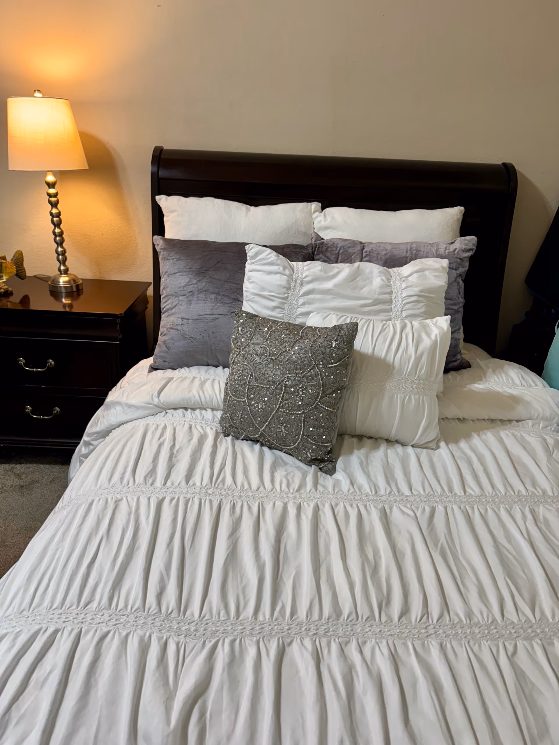 Bedroom featuring a dark headboard, white bedding, pillows, nightstand, and lamp.