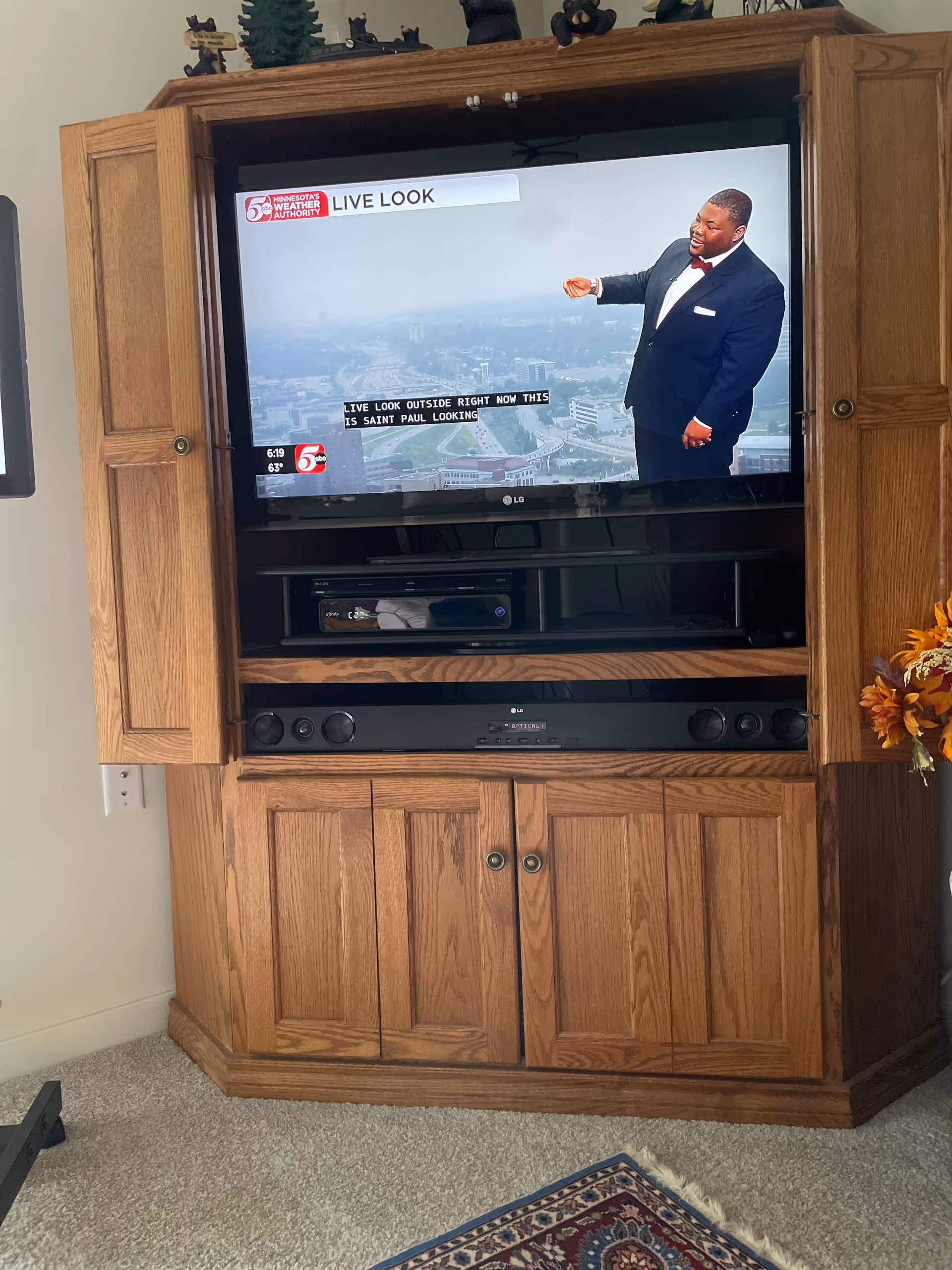 Wooden corner entertainment center with a TV showing a man in a suit.