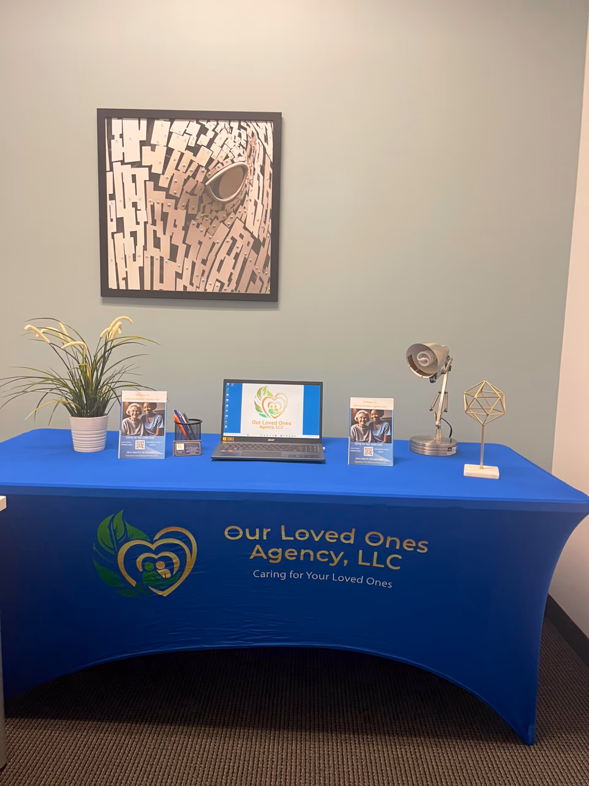 Blue-covered information desk with laptop, brochures, plant, and a desk lamp.