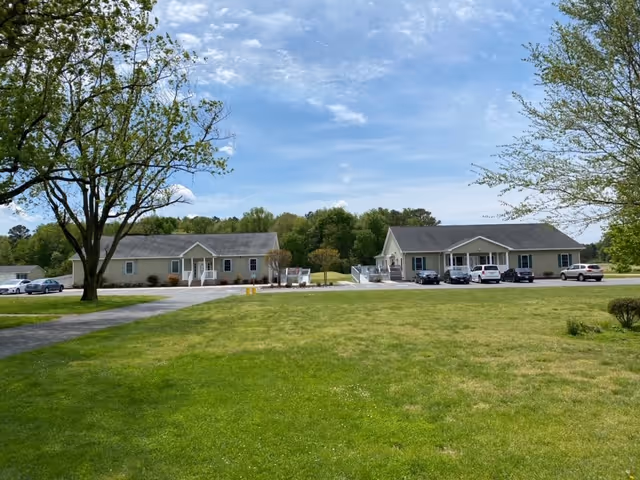 Wide view of Delmar Villa Assisted Living campus with two beige front buildings and parking lot.