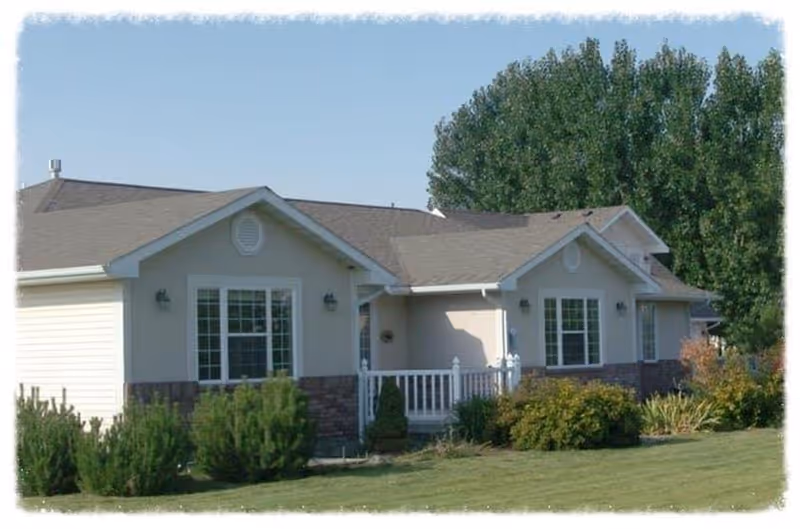 Single-story light-colored assisted living building with a small front porch, lawn and shrubs