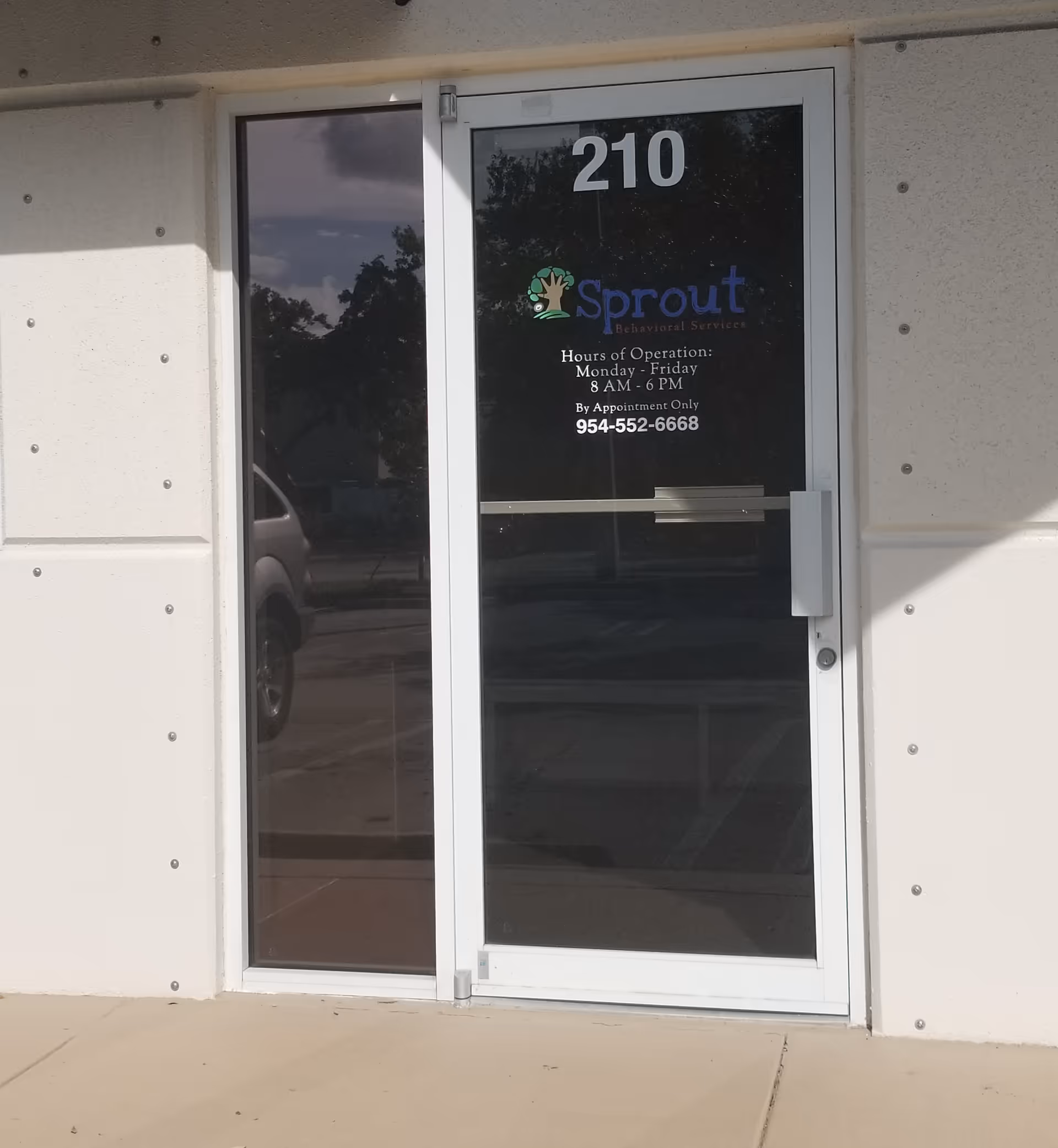 Glass door entry with Sprout Behavioral Services logo and the number 210 on beige wall.