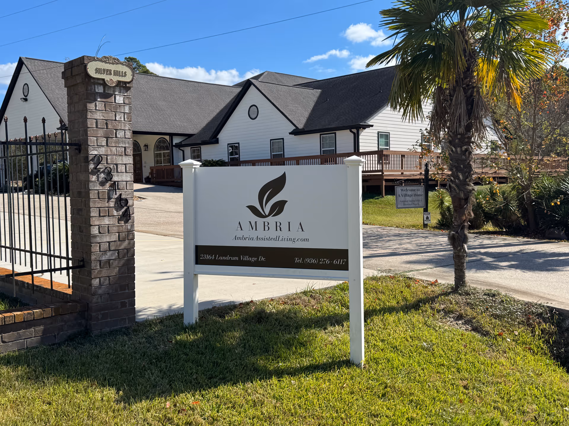 Front exterior view of Ambria Assisted Living with sign, palm tree, and building.