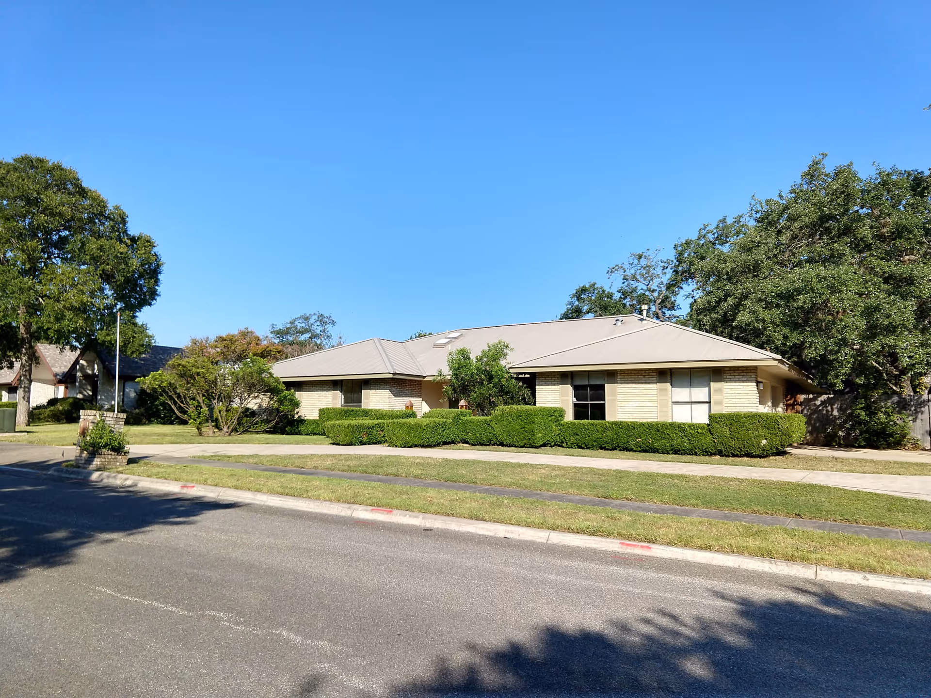 Front view of a single-story memory care building with trimmed hedges and trees.