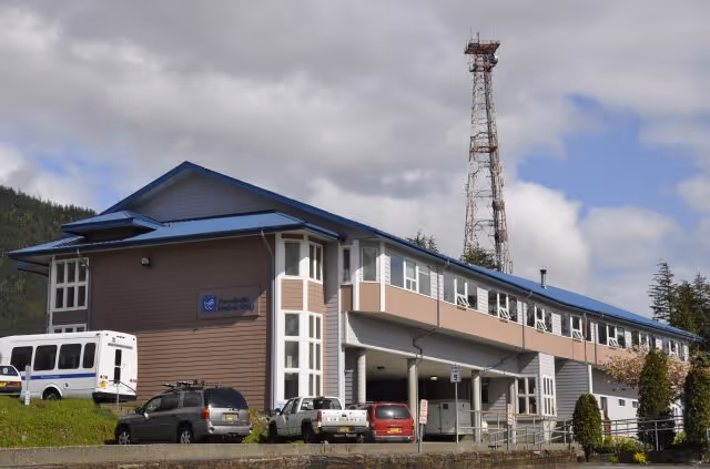 Exterior view of a two-story PeaceHealth facility with blue roof, parked vehicles, and a tall tower.