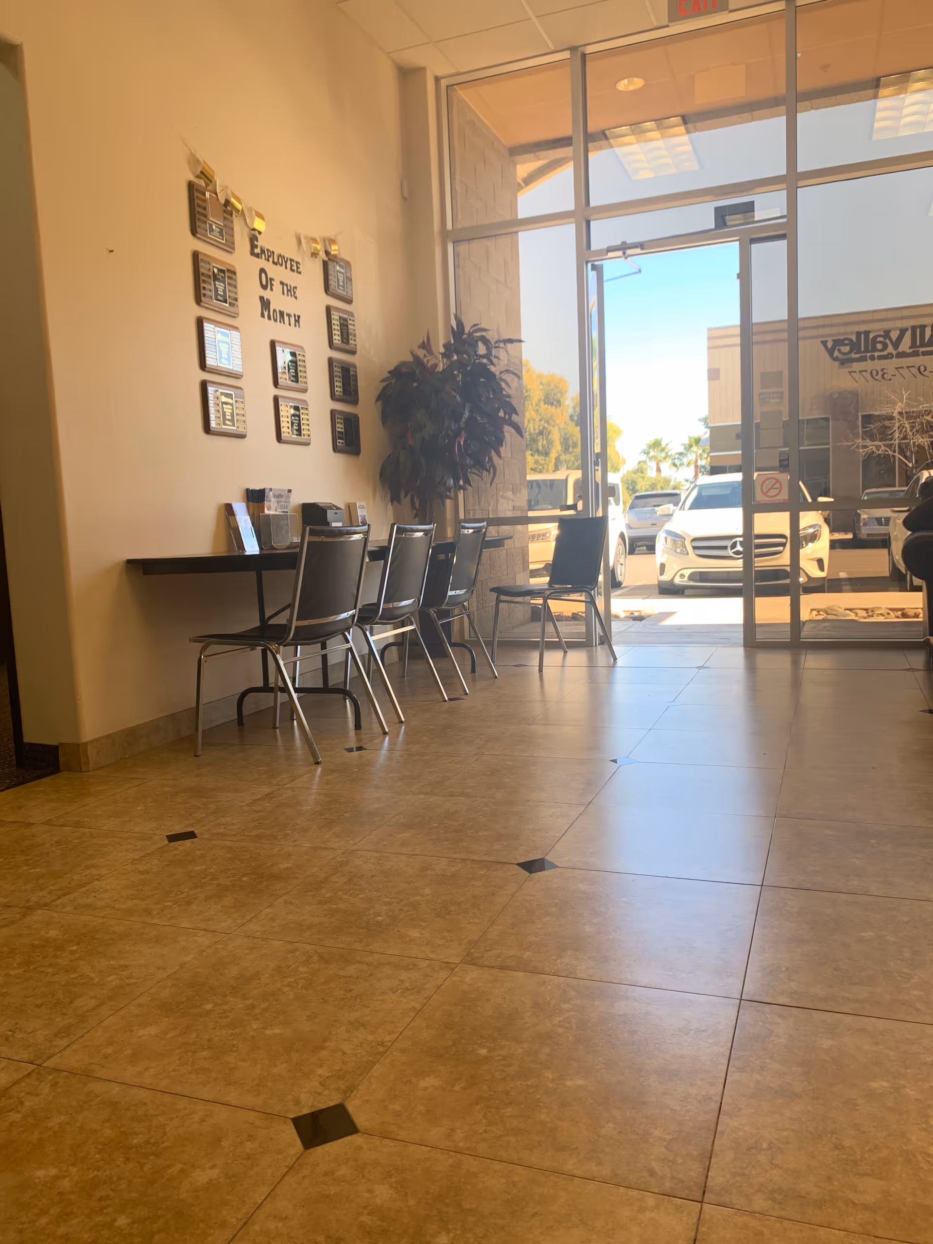 Lobby area with chairs, a desk, and Employee of the Month plaques near glass doors.