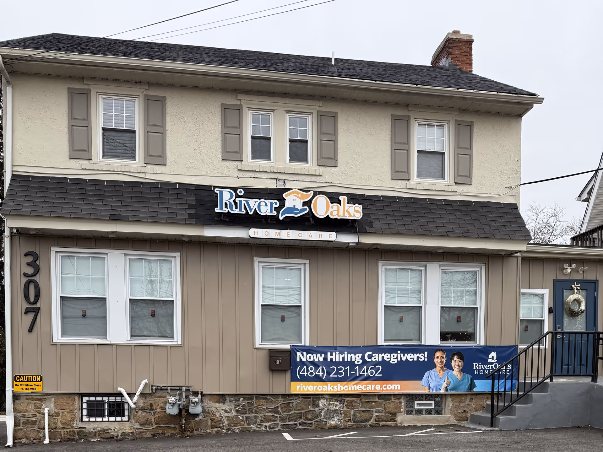 Two-story beige River Oaks Home Care building with sign and recruitment banner.
