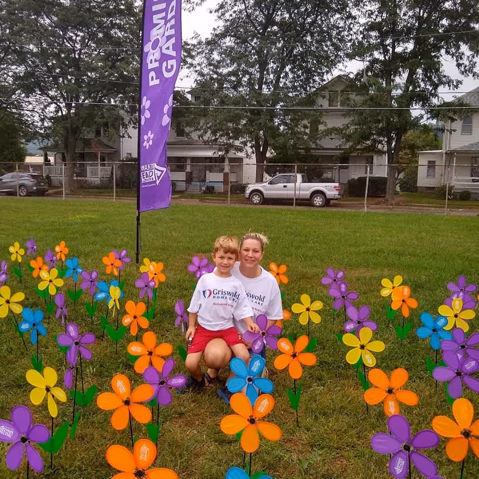 Two people kneel among colorful pinwheels in a grassy outdoor area.