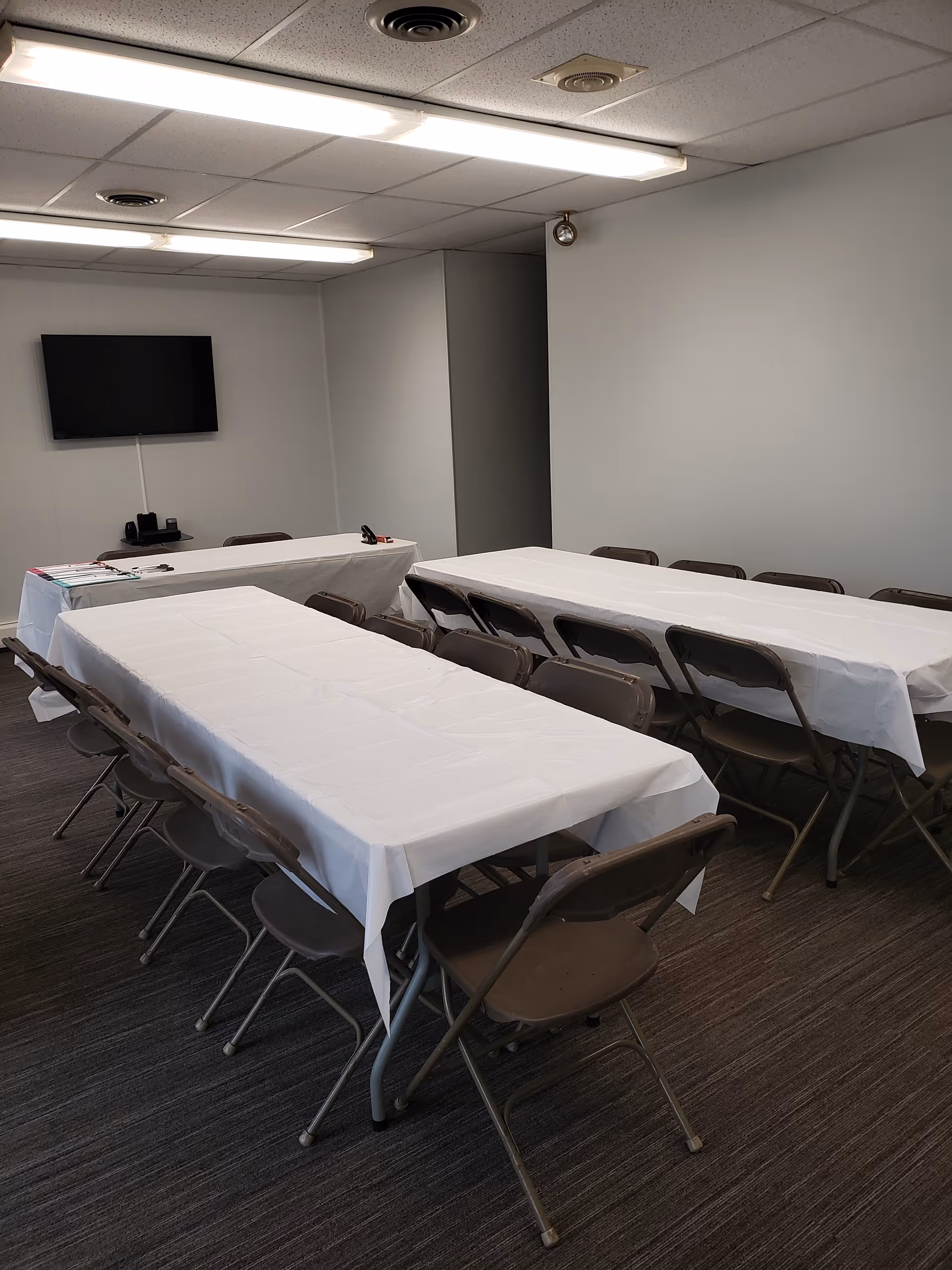 An interior conference room with white tablecloths on folding tables and brown chairs.