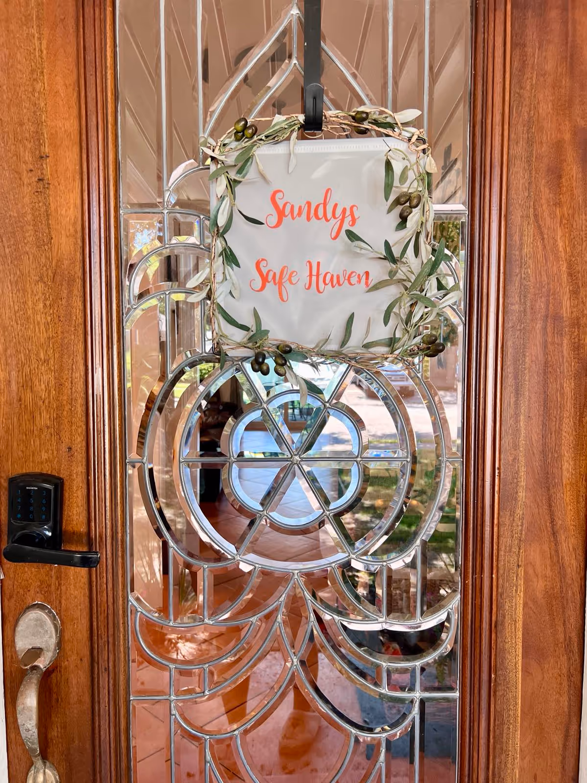 Wooden front door with decorative glass and a wreath reading 'Sandy's Safe Haven'.