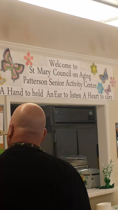 Bald man facing away inside St. Mary Parish Council on Aging, near a welcoming sign.