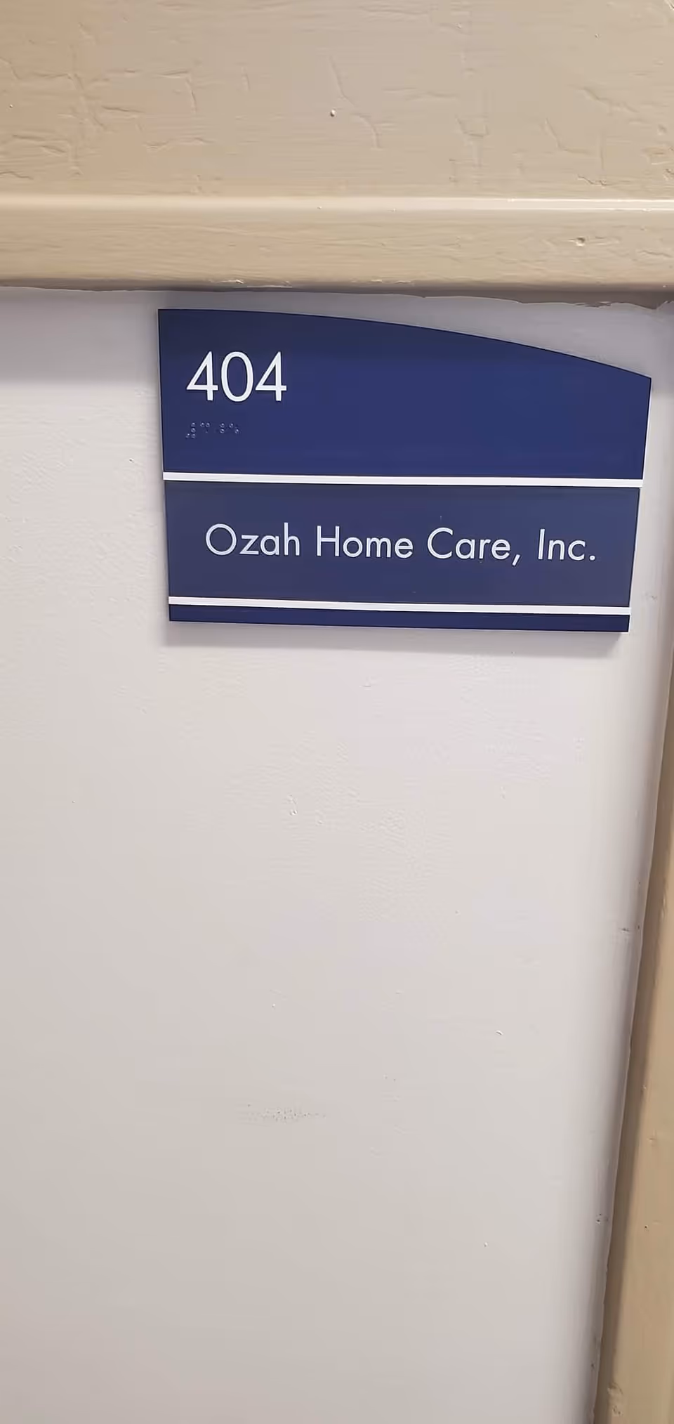 Blue wall placard showing 404 and Ozah Home Care, Inc., mounted on a white hallway wall.
