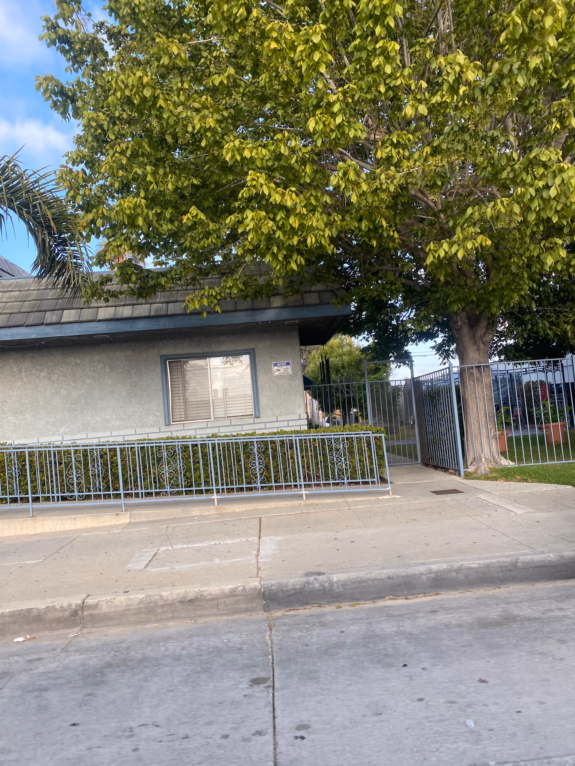 Exterior view of a single-story Americare Assisted Living building with a metal fence and trees.