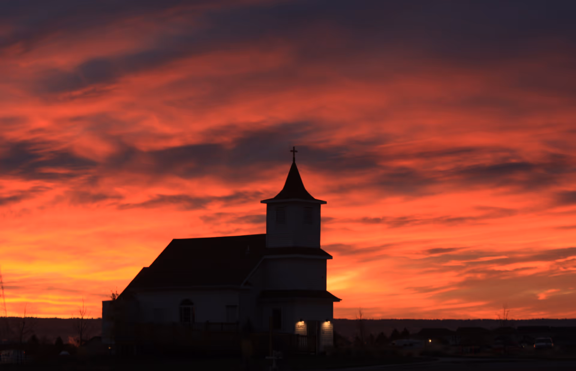Silhouetted church with steeple against a dramatic red sunset sky.