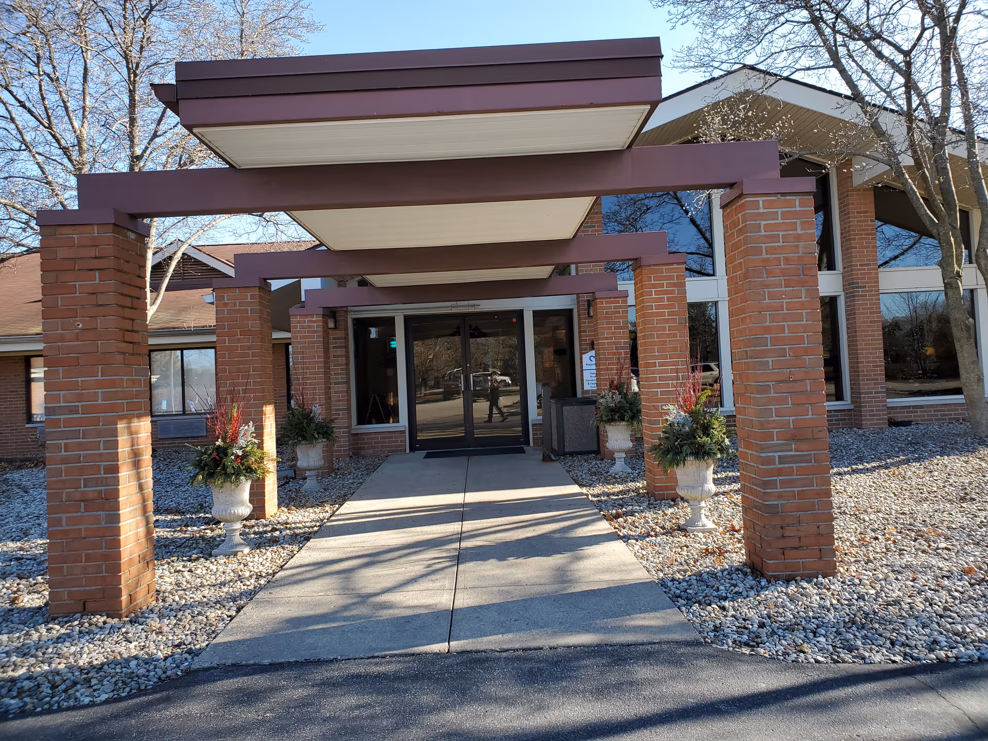 Brick facility entrance with a covered portico and potted plants.