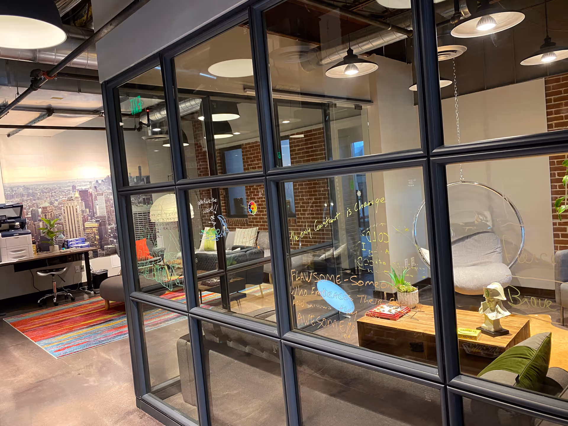 Glass-walled lounge with chairs, a hanging pod chair, and a city mural.