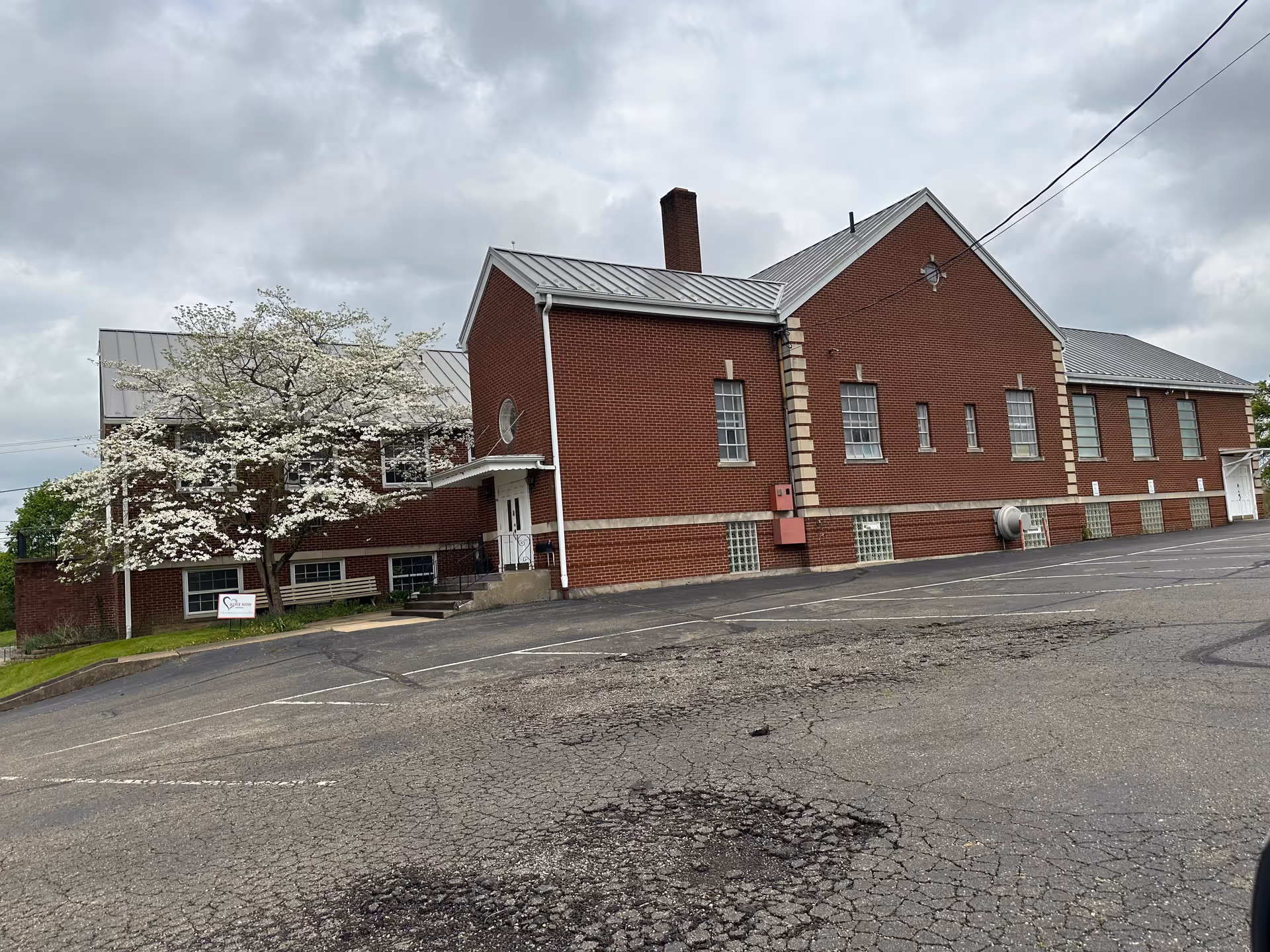 The brick senior living facility exterior shows a blooming tree and an empty parking lot.