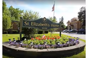 Circular flower bed with a St. Elizabeth's Home sign and building in the background