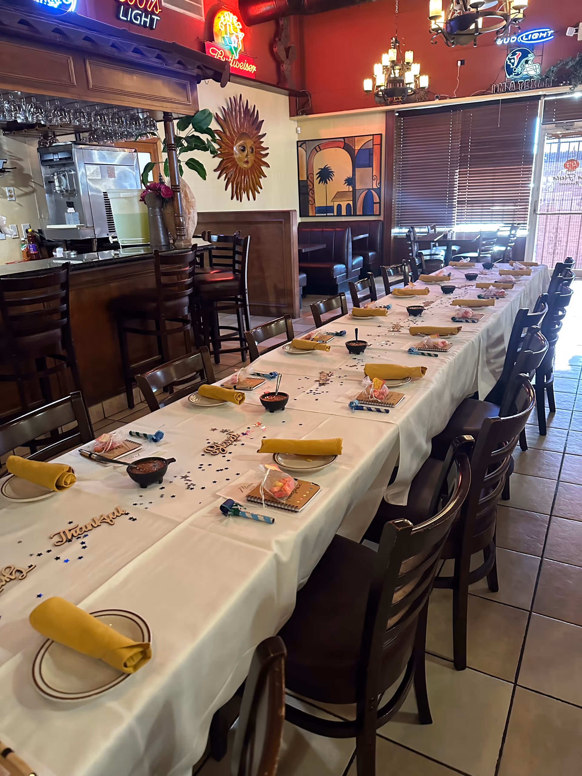 Long dining table in a restaurant set with yellow napkins and place settings.