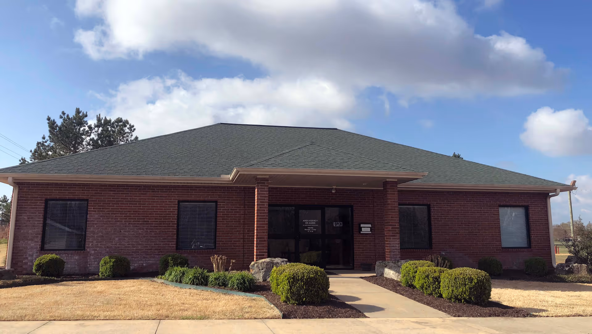 Brick office building with a central front entrance and trimmed shrubs.
