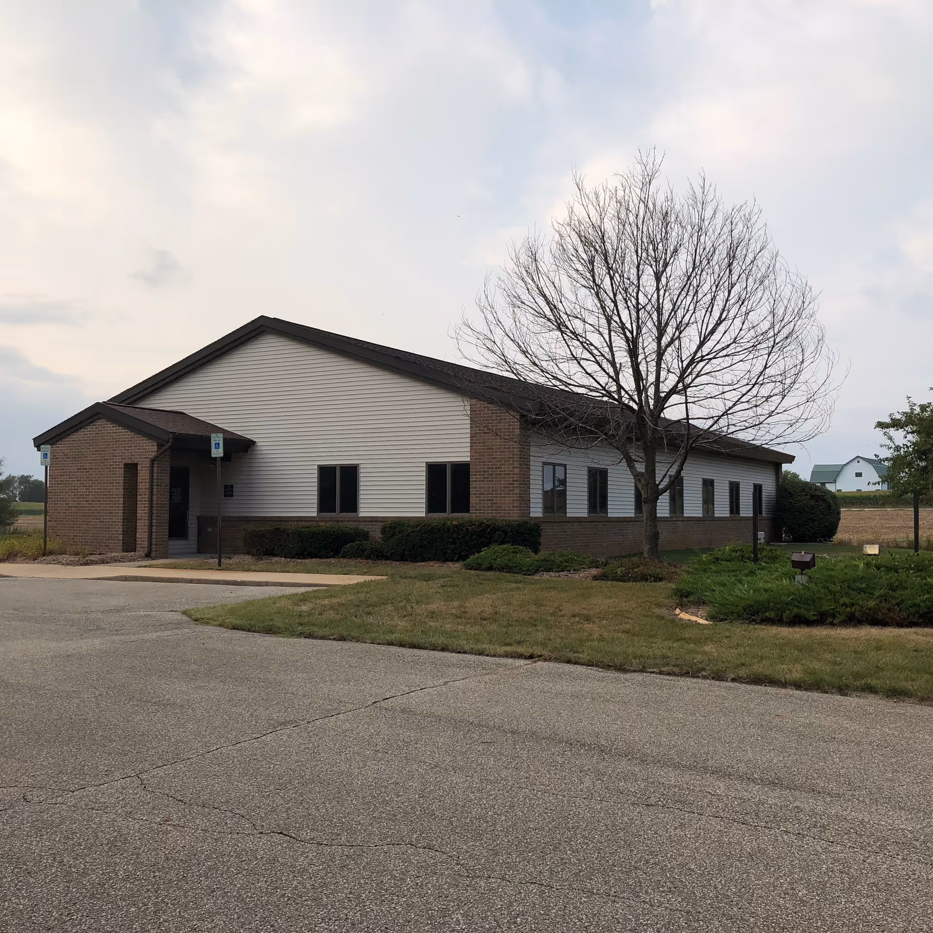 Single-story brick and siding building with a leafless tree in front and a paved parking area.
