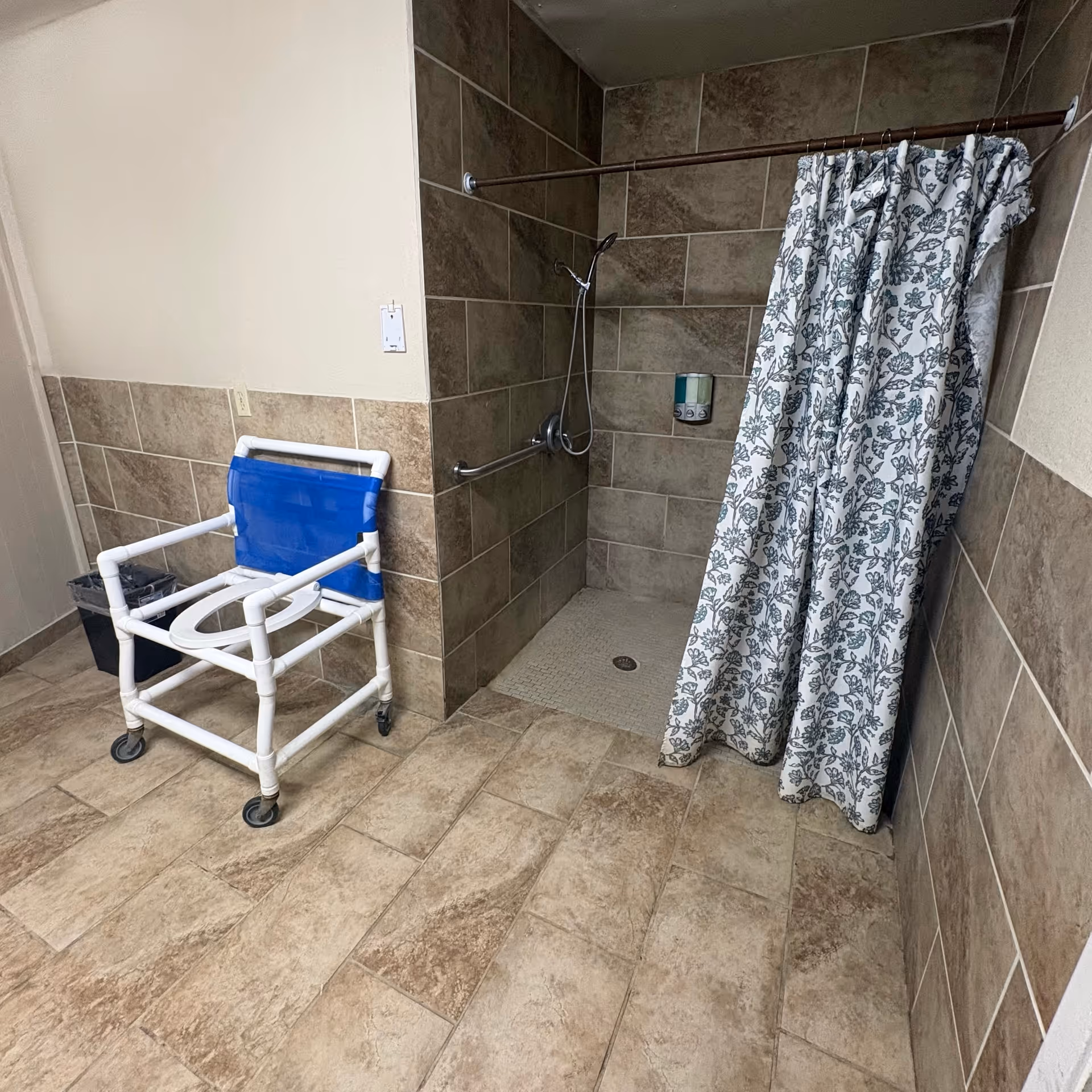 Accessible bathroom with blue shower chair, tiled walls, and a patterned shower curtain.