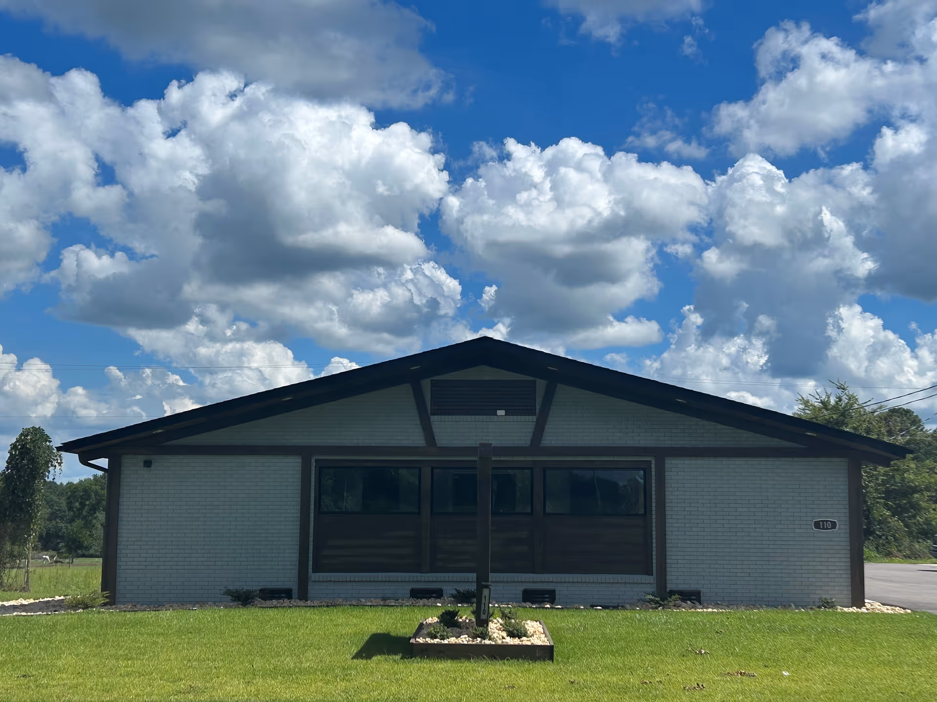 Single-story brick facility with large front windows, dark trim, and a manicured lawn under cloudy sky.