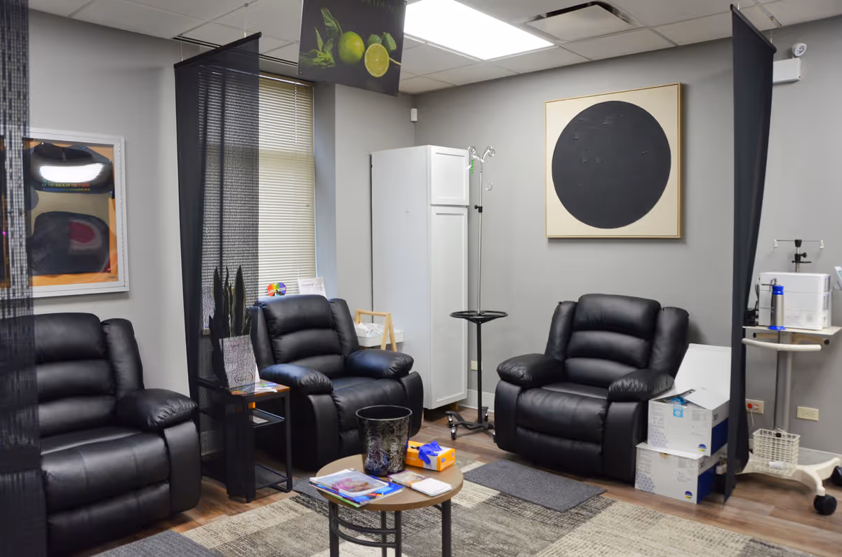 A medical lounge with black leather recliners, dividers, and a small table in a common area.