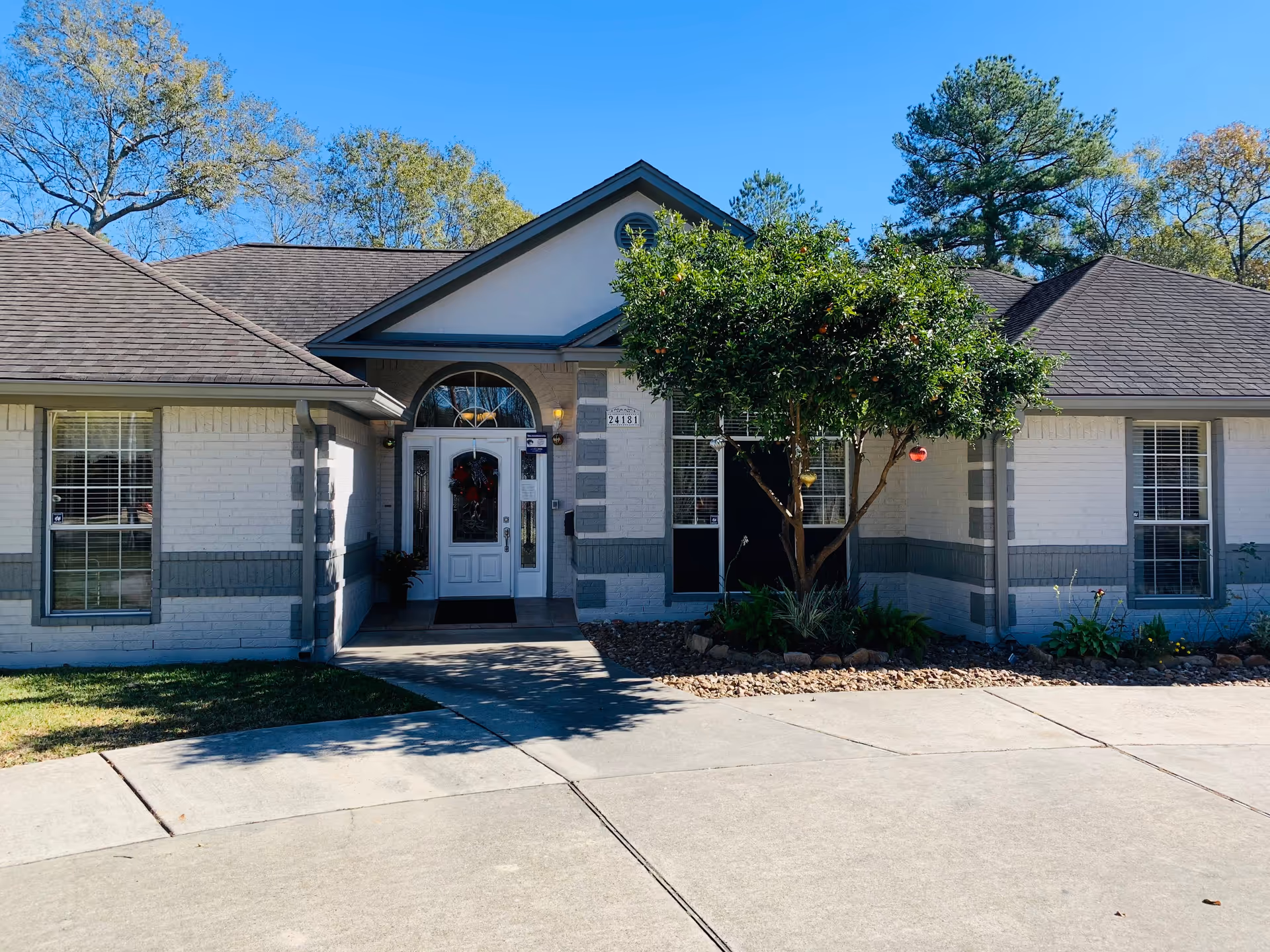 Front exterior of a single-story brick senior care home with a central entrance, windows, and a small tree in the front yard.