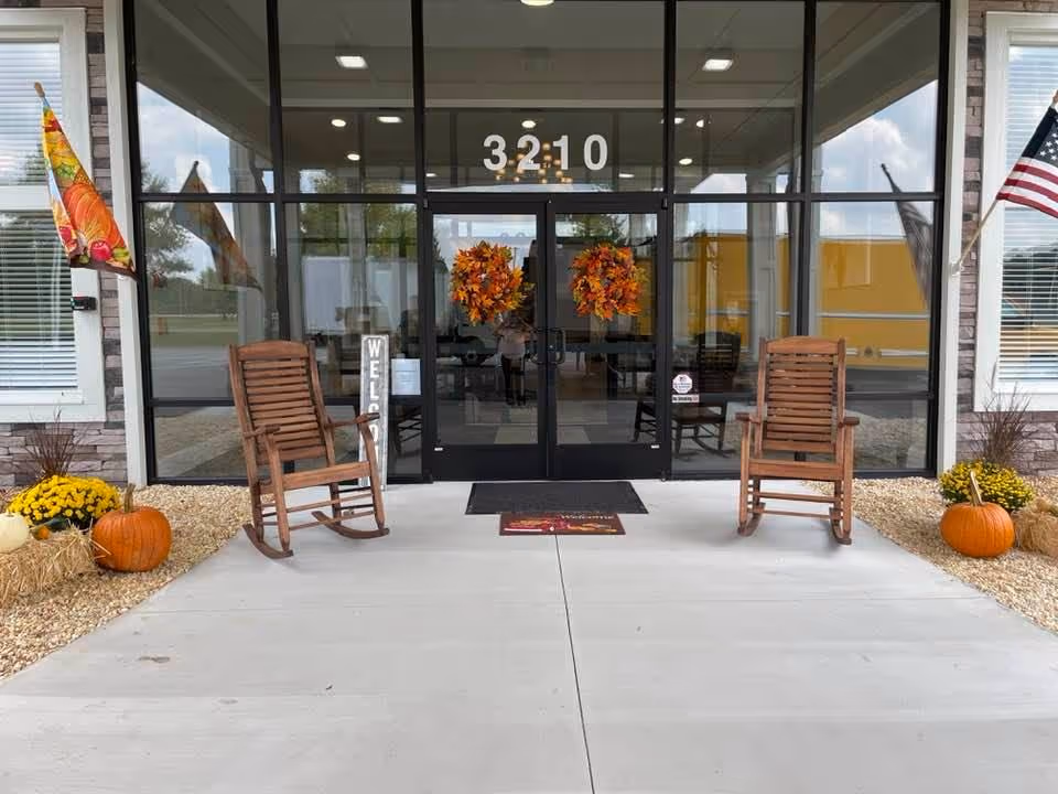 Front entrance of Open Fields Assisted Living with glass doors, rocking chairs, pumpkins, and autumn decor.