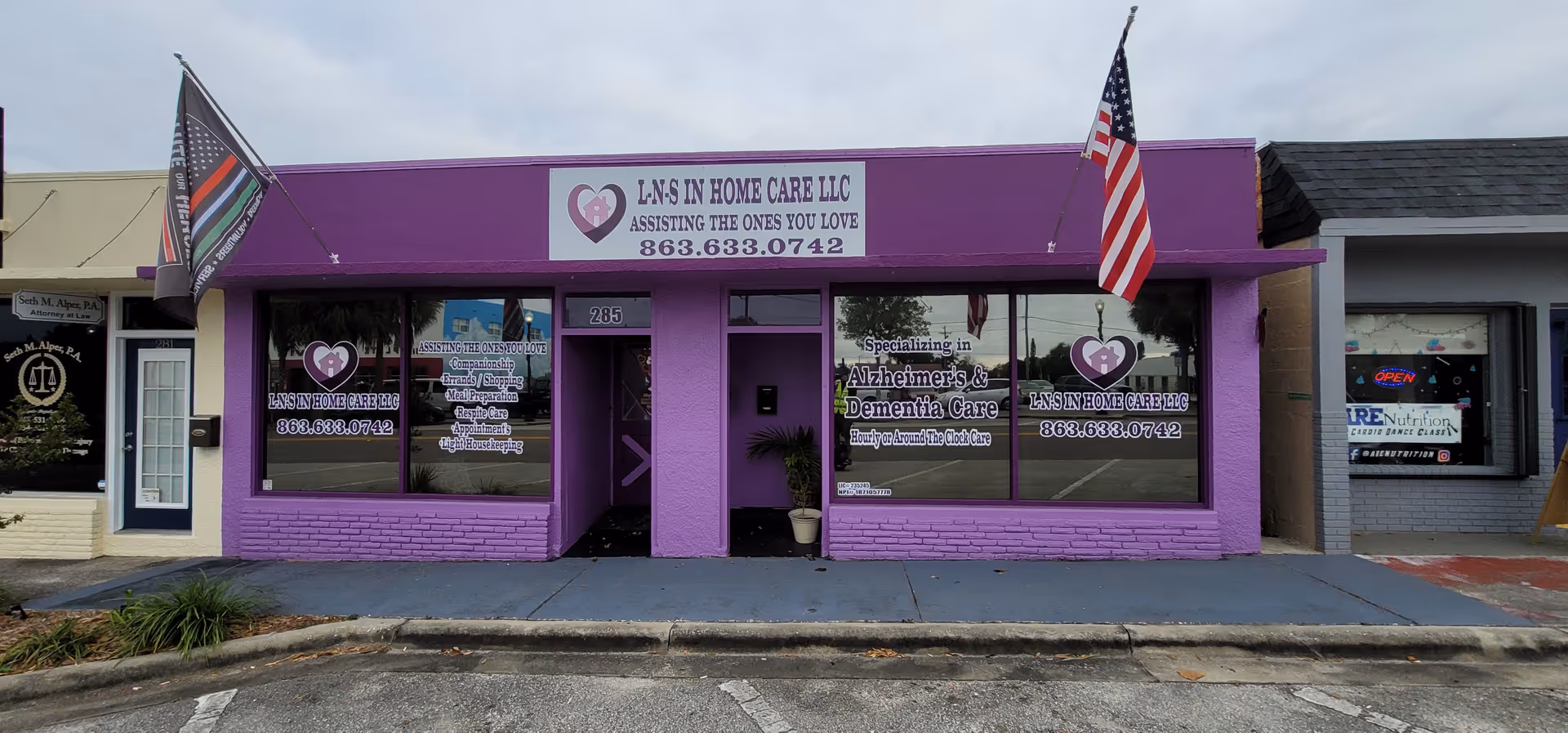 Purple storefront for L-N-S In Home Care LLC with flags and large windows.