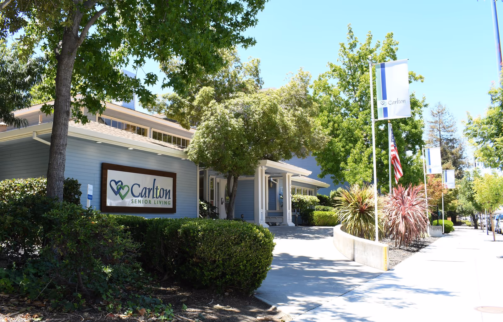 Front view of Carlton Senior Living building with sign, trees, and sidewalk.