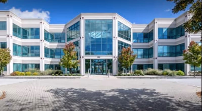 Modern glass-front senior living facility exterior with a central entrance and landscaping.