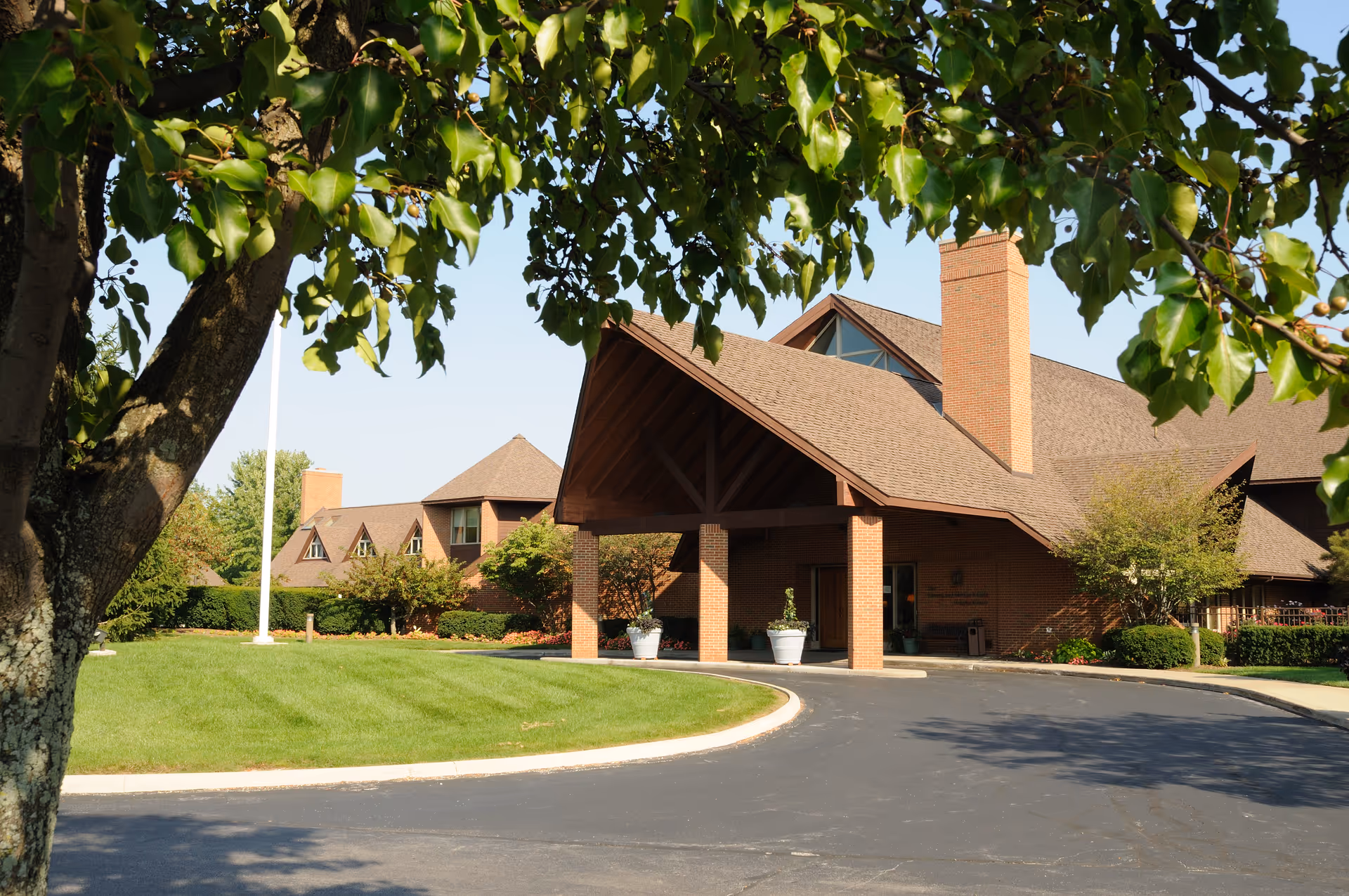Hospice of Northwest Ohio entrance under a peaked roof, brick building, circular driveway, trees.